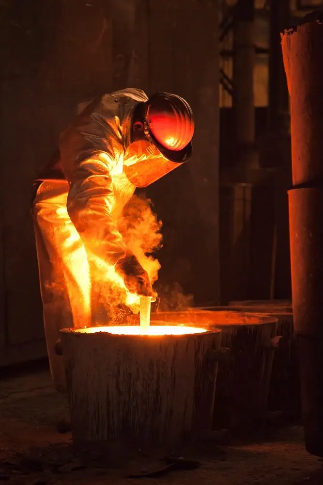 A worker in heat gear beside a crucible of molten metal
